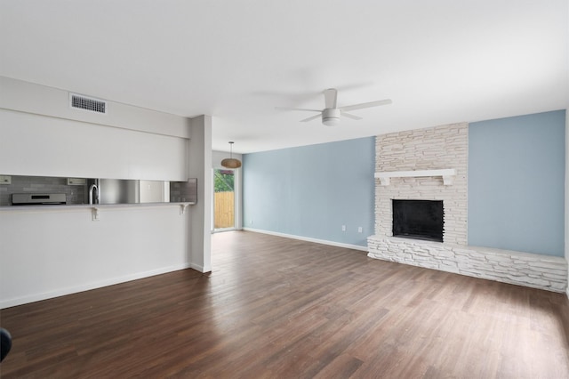 unfurnished living room featuring ceiling fan, a stone fireplace, and dark hardwood / wood-style floors