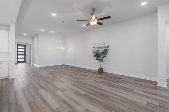 empty room featuring ceiling fan with notable chandelier and light hardwood / wood-style floors