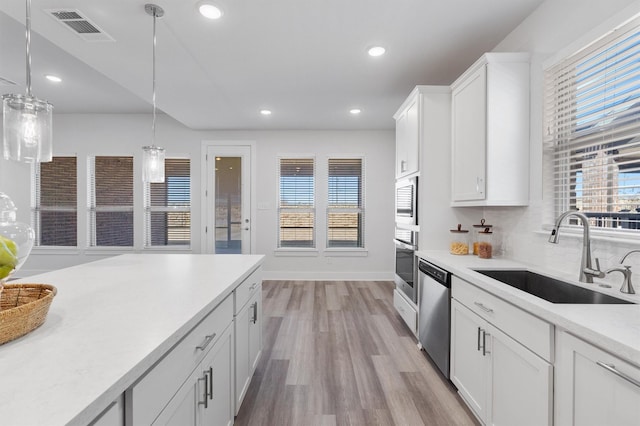 kitchen with sink, white cabinets, decorative light fixtures, light wood-type flooring, and appliances with stainless steel finishes