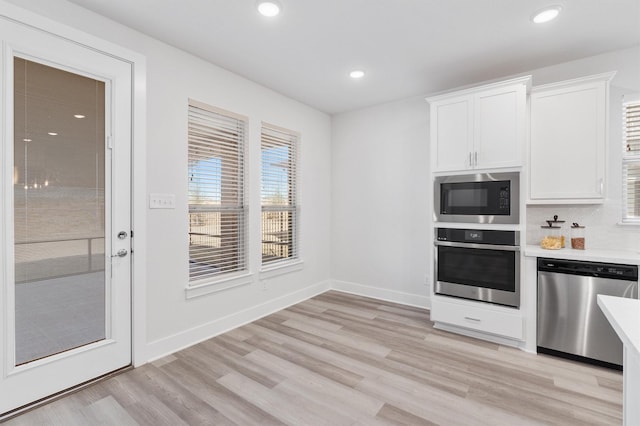 kitchen featuring stainless steel appliances, white cabinetry, light wood-type flooring, and tasteful backsplash