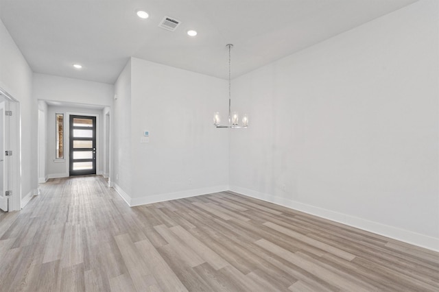 spare room featuring light wood-type flooring and an inviting chandelier