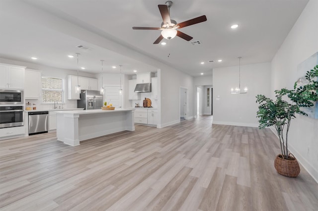 kitchen with appliances with stainless steel finishes, pendant lighting, a kitchen island, white cabinets, and light hardwood / wood-style flooring