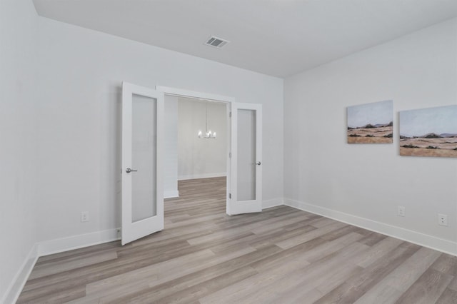 unfurnished room with light hardwood / wood-style floors, french doors, and a notable chandelier