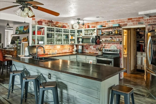 kitchen featuring dark countertops, a breakfast bar, a peninsula, stainless steel appliances, and a sink