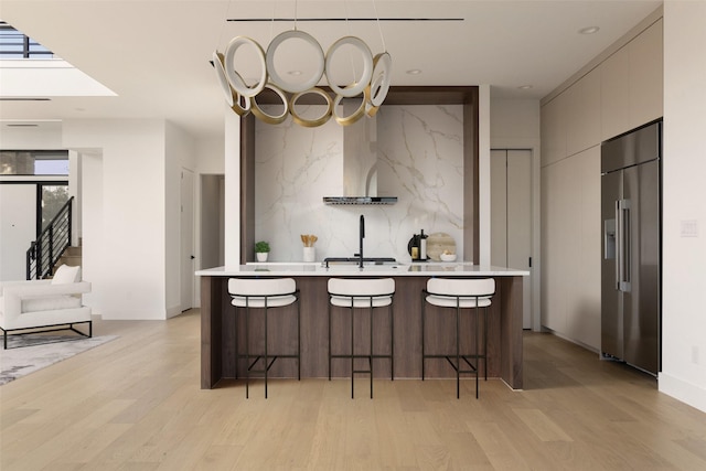 kitchen with a breakfast bar, light wood-type flooring, built in refrigerator, and decorative backsplash