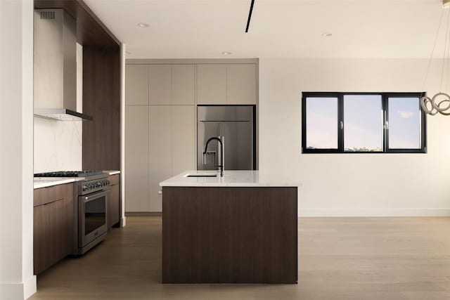 kitchen with stainless steel appliances, light wood-type flooring, a kitchen island with sink, and wall chimney exhaust hood