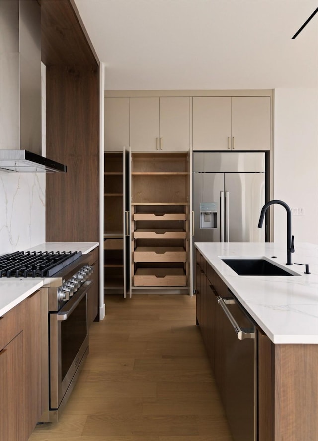 kitchen featuring light hardwood / wood-style floors, stainless steel appliances, decorative backsplash, wall chimney exhaust hood, and sink