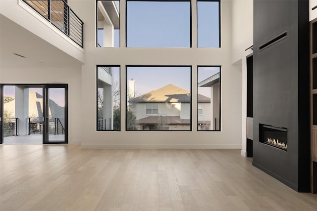 unfurnished living room featuring a towering ceiling, a fireplace, and light hardwood / wood-style flooring