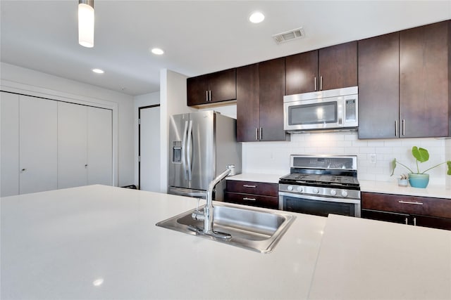 kitchen featuring sink, backsplash, dark brown cabinets, hanging light fixtures, and appliances with stainless steel finishes