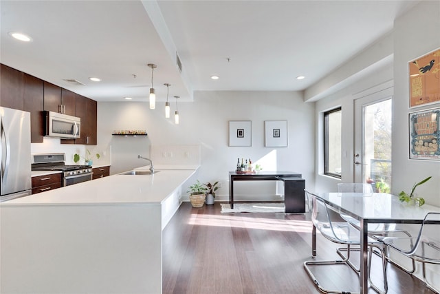 kitchen featuring sink, appliances with stainless steel finishes, hanging light fixtures, dark brown cabinets, and dark wood-type flooring