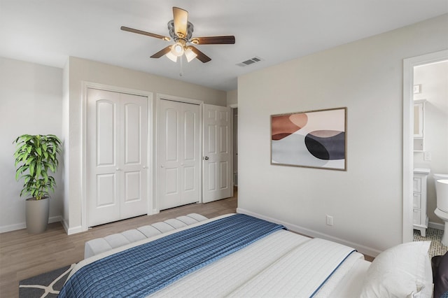 bedroom featuring ensuite bathroom, ceiling fan, light hardwood / wood-style floors, and two closets