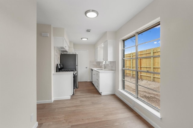 kitchen featuring backsplash, light wood-type flooring, stainless steel gas stove, white cabinets, and sink