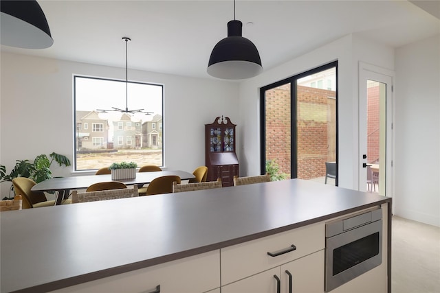 kitchen featuring decorative light fixtures, white cabinets, stainless steel microwave, and a healthy amount of sunlight