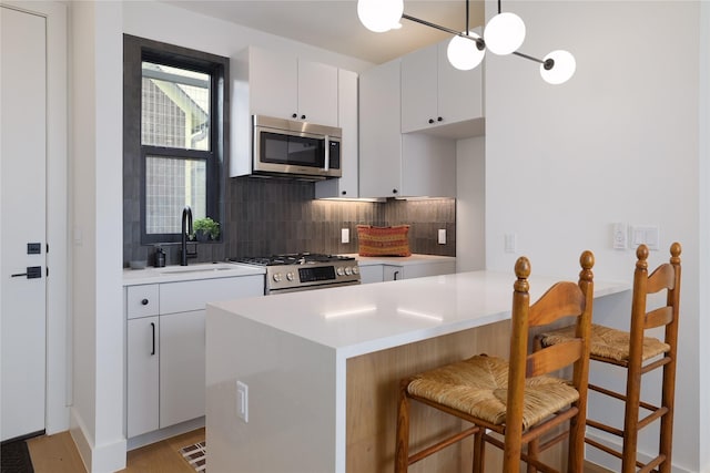 kitchen with appliances with stainless steel finishes, a breakfast bar, white cabinets, and tasteful backsplash