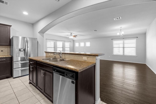 kitchen with sink, stainless steel appliances, a center island with sink, ceiling fan with notable chandelier, and dark brown cabinetry