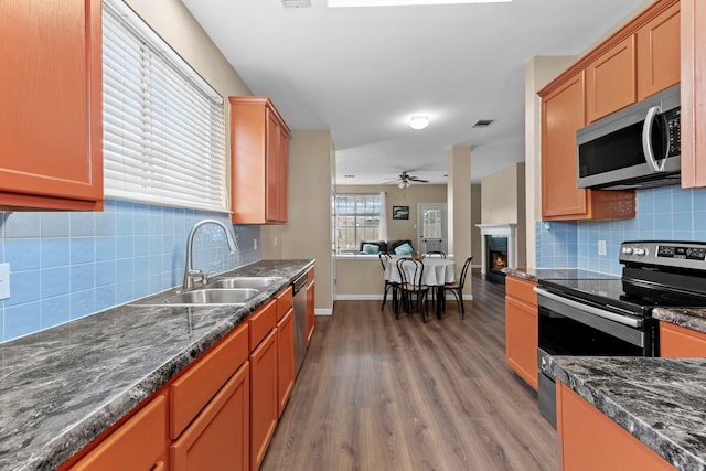 kitchen with stainless steel appliances, sink, dark stone countertops, ceiling fan, and dark wood-type flooring