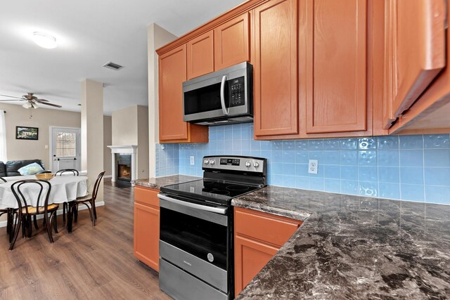 kitchen with ceiling fan, tasteful backsplash, dark stone countertops, wood-type flooring, and appliances with stainless steel finishes