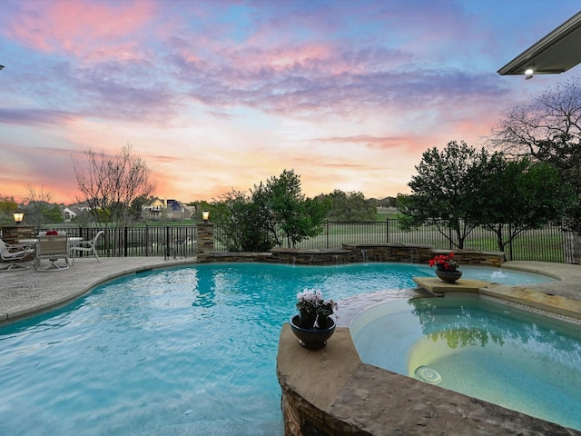 pool at dusk with pool water feature, a patio area, and an in ground hot tub