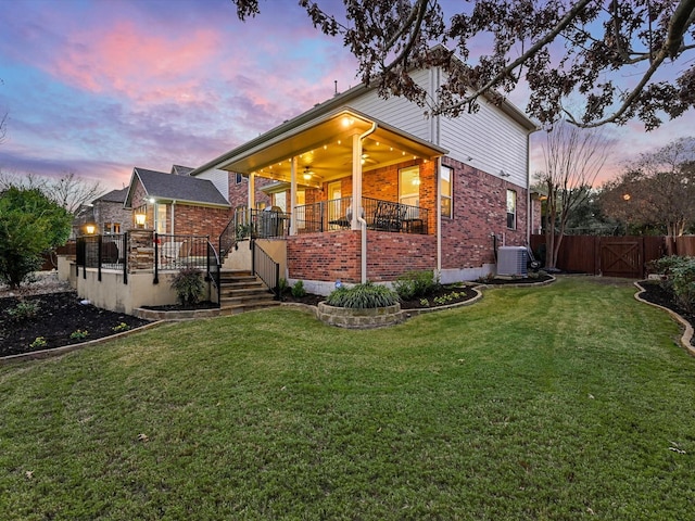 back house at dusk with a lawn, ceiling fan, and central AC unit