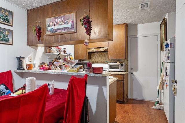 kitchen featuring white refrigerator, a textured ceiling, a kitchen breakfast bar, kitchen peninsula, and wood-type flooring