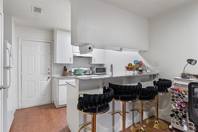 kitchen with kitchen peninsula, a textured ceiling, white fridge, a breakfast bar area, and white cabinets