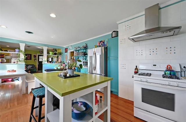 kitchen featuring wall chimney range hood, crown molding, light hardwood / wood-style flooring, stainless steel appliances, and a kitchen bar