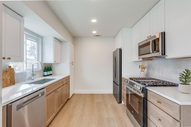 kitchen featuring light hardwood / wood-style floors, backsplash, white cabinets, appliances with stainless steel finishes, and sink