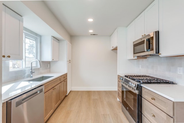 kitchen featuring stainless steel appliances, light hardwood / wood-style floors, tasteful backsplash, white cabinets, and sink