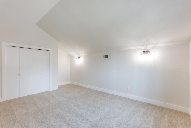 unfurnished bedroom with vaulted ceiling, light colored carpet, and a closet