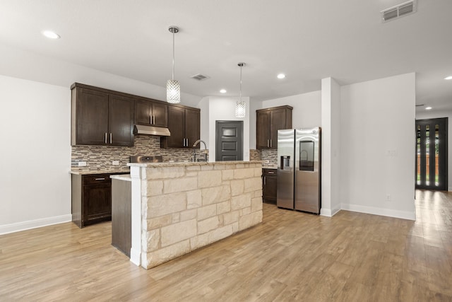 kitchen with a center island with sink, stainless steel fridge with ice dispenser, pendant lighting, dark brown cabinetry, and backsplash