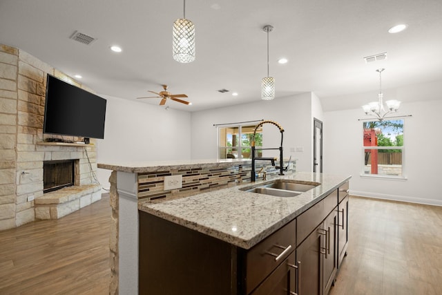 kitchen featuring sink, hanging light fixtures, a stone fireplace, and ceiling fan with notable chandelier