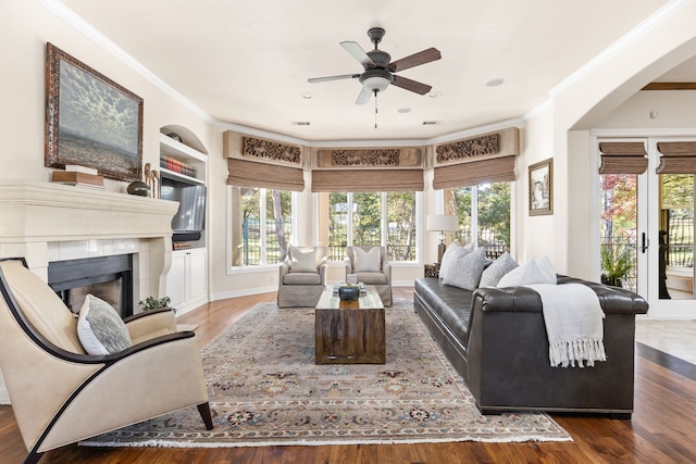 living room with a tiled fireplace, ceiling fan, built in features, and dark wood-type flooring