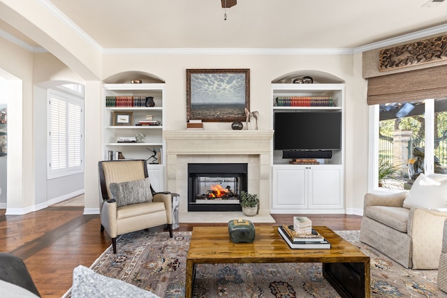 living room with a tile fireplace, built in features, ceiling fan, and crown molding