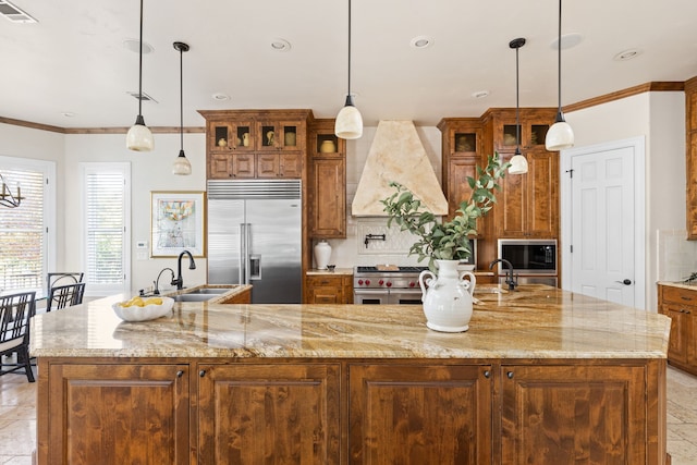 kitchen featuring a large island with sink, built in appliances, premium range hood, sink, and tasteful backsplash