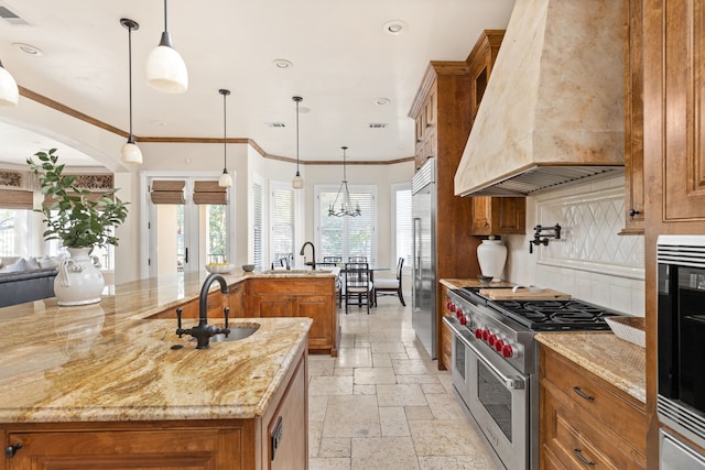 kitchen featuring a large island with sink, premium appliances, custom range hood, and hanging light fixtures