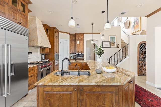 kitchen featuring a kitchen island with sink, hanging light fixtures, light stone countertops, premium range hood, and high quality appliances