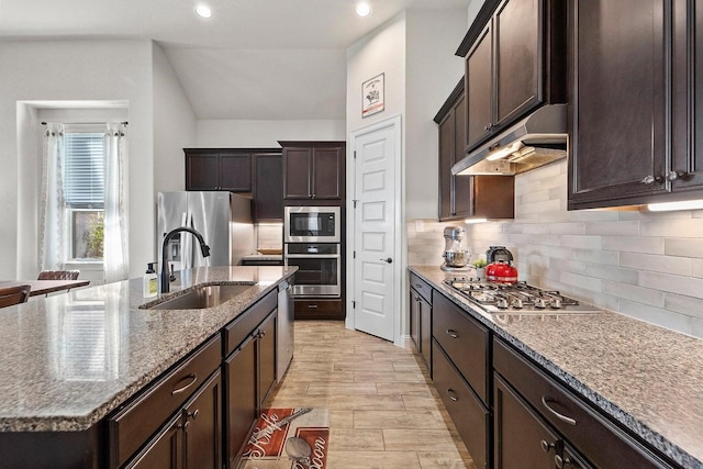 kitchen with stainless steel appliances, backsplash, a kitchen island with sink, light stone counters, and sink