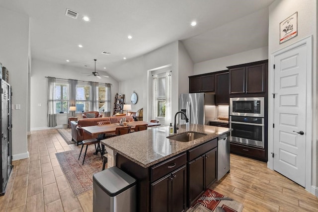 kitchen featuring ceiling fan, appliances with stainless steel finishes, a kitchen island with sink, light stone counters, and sink