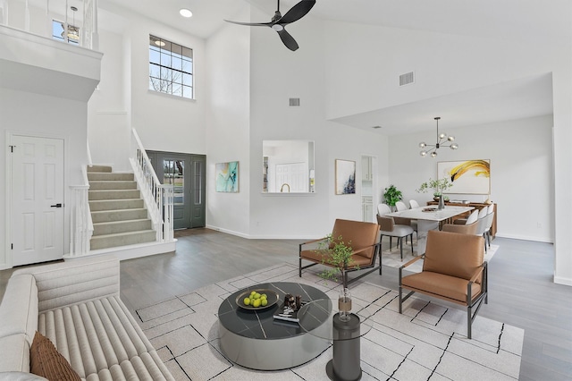 living room with ceiling fan with notable chandelier, a towering ceiling, and light hardwood / wood-style floors