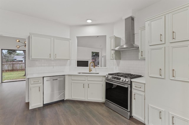 kitchen with appliances with stainless steel finishes, dark wood-type flooring, white cabinets, wall chimney range hood, and sink