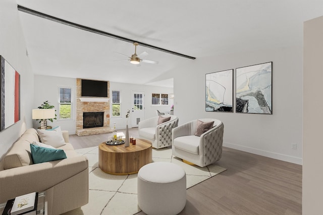 living room featuring lofted ceiling, hardwood / wood-style flooring, ceiling fan, and a stone fireplace