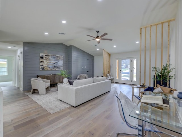 living room featuring recessed lighting, visible vents, light wood-style flooring, vaulted ceiling, and wooden walls