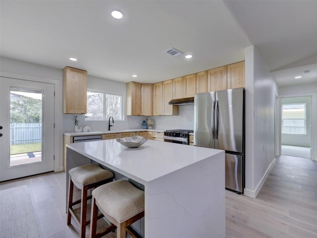 kitchen with a breakfast bar area, stainless steel appliances, visible vents, light brown cabinets, and a sink