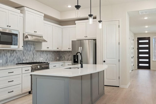 kitchen featuring decorative light fixtures, stainless steel appliances, an island with sink, and white cabinets