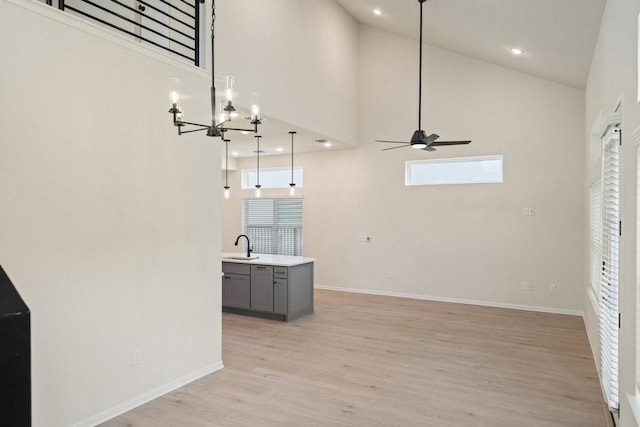 unfurnished living room featuring sink, ceiling fan with notable chandelier, light hardwood / wood-style floors, and a high ceiling