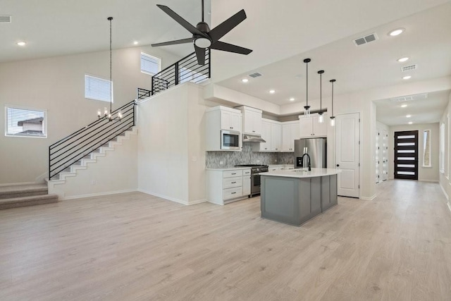 kitchen featuring light hardwood / wood-style flooring, appliances with stainless steel finishes, hanging light fixtures, an island with sink, and white cabinets