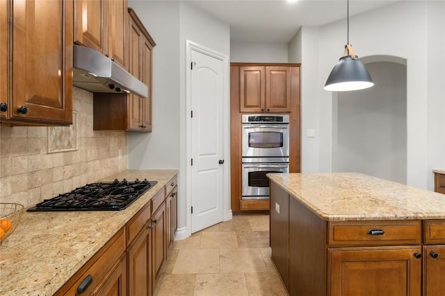 kitchen featuring under cabinet range hood, stainless steel double oven, black gas cooktop, decorative backsplash, and light stone counters