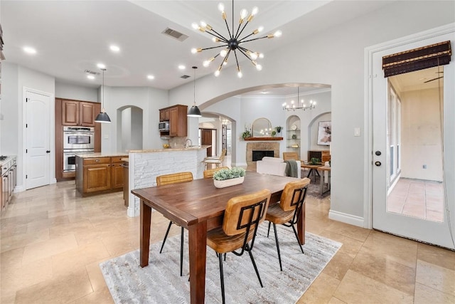 dining room featuring arched walkways, a chandelier, a fireplace, light tile patterned floors, and ornamental molding