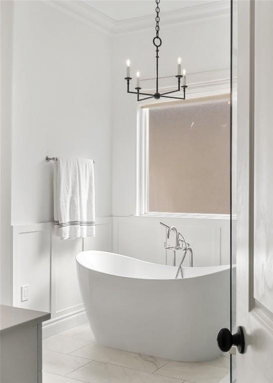 bathroom with a chandelier, ornamental molding, a decorative wall, wainscoting, and a soaking tub