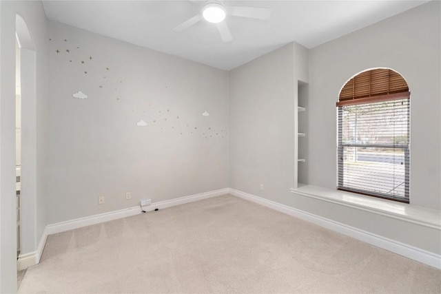 empty room featuring light carpet, a ceiling fan, baseboards, and arched walkways